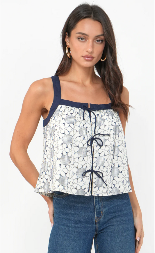 Woman wearing a floral top with navy straps and blue jeans on a white background