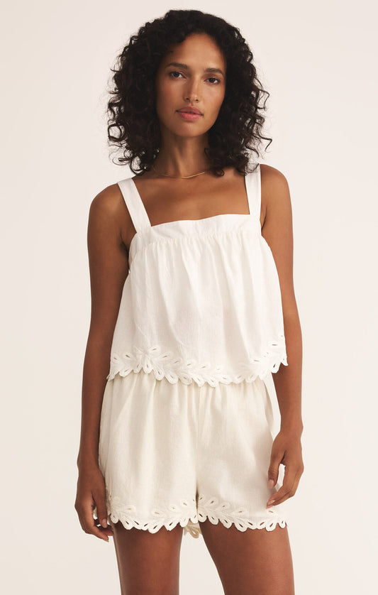 Woman wearing a white romper top and bottom with pretty details on a plain background