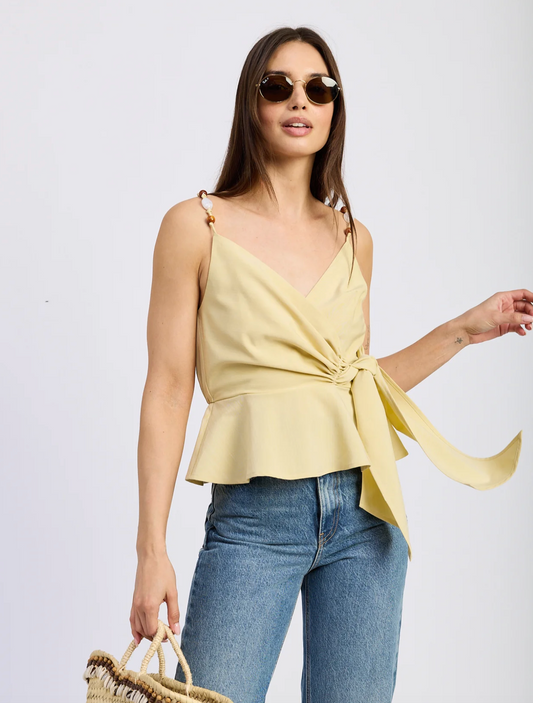 Woman wearing a yellow top and blue jeans with sunglasses on a white background