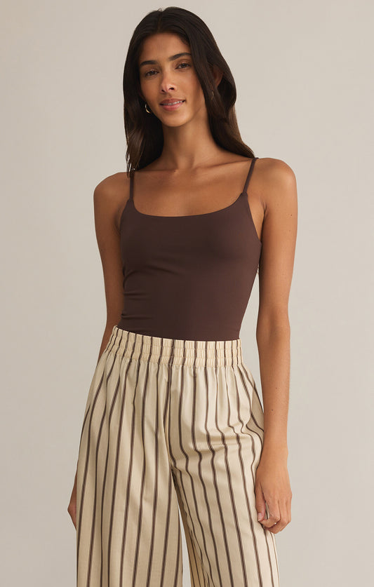 A woman wearing a brown Luxe Smooth Jersey Bodysuit with thin straps, paired with striped trousers.