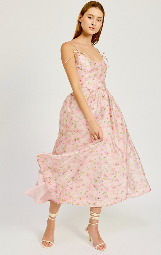 A female model wearing a midi length, floral print dress with a sleeveless design and light pink color.