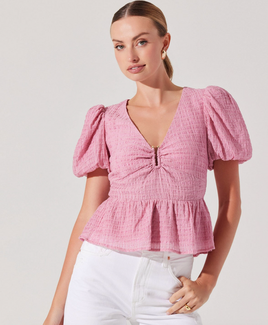 A woman wearing a pink short sleeve top with a V-neckline and puff sleeves, paired with white trousers.