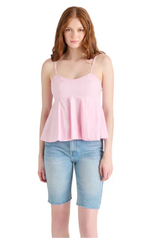 A woman wearing a pink sleeveless top with a peplum and spaghetti straps, paired with blue denim shorts.