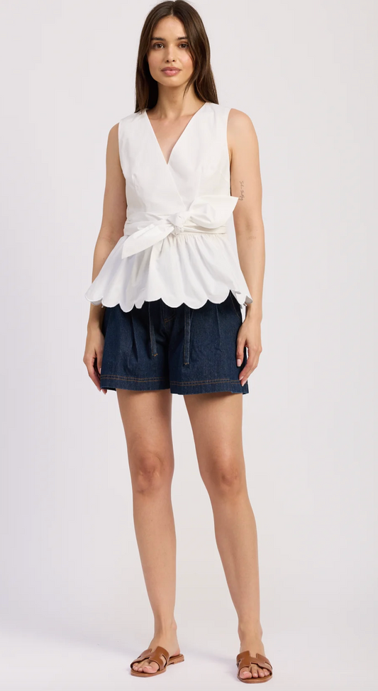 Woman wearing a white peplum top and dark shorts on a white background