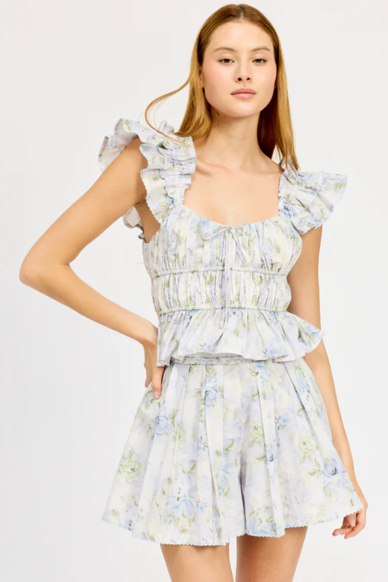 A female model wearing a short sleeve floral top with a ruffled design and a matching floral skirt.