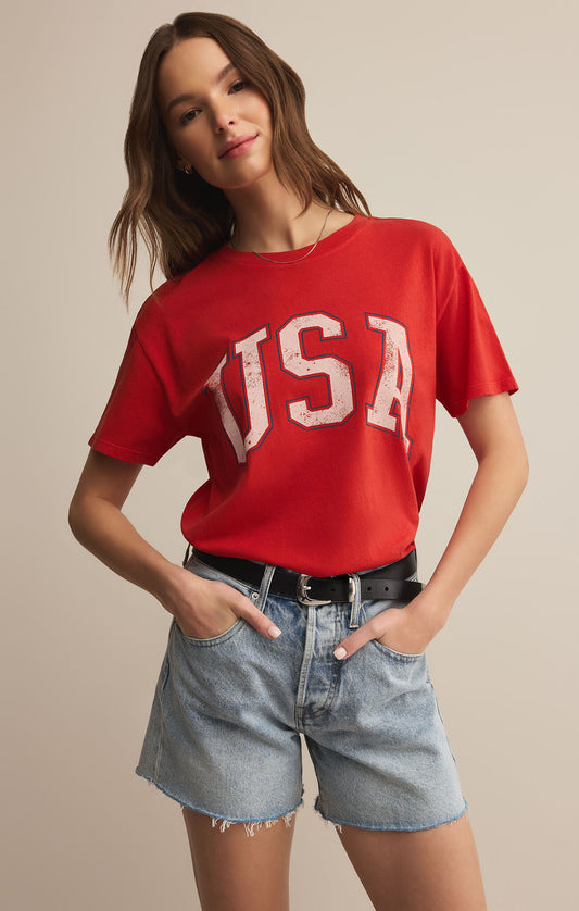 Person wearing a red 'USA' t-shirt and denim shorts on a beige background