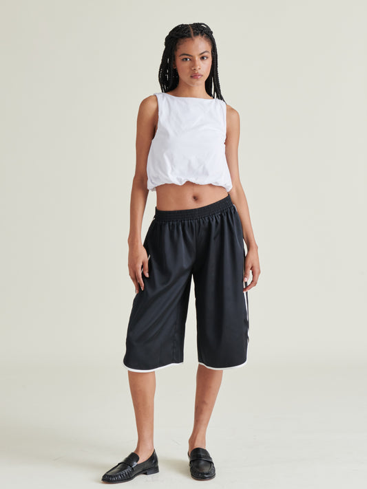 Person wearing a white sleeveless top and black wide-leg pants on a plain background