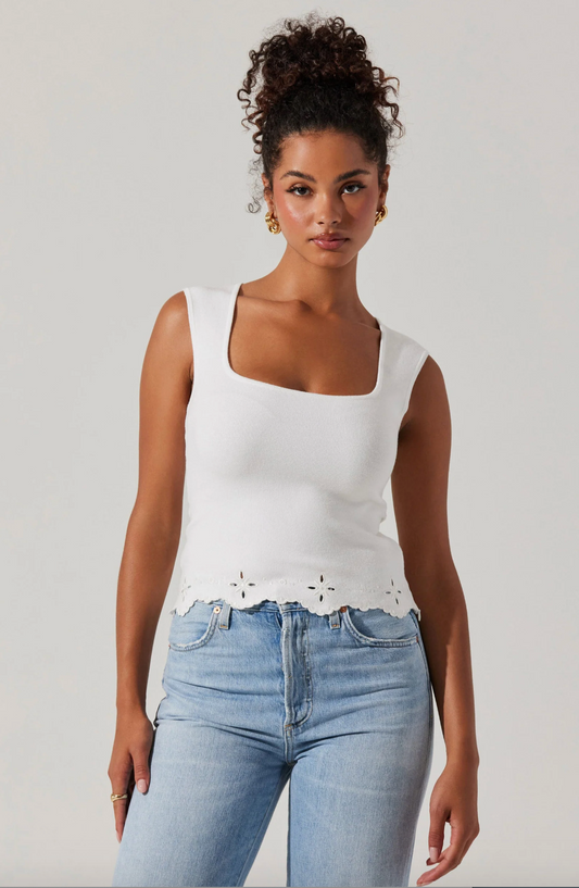 Woman wearing a white sleeveless top with lace details and light blue jeans on a plain background