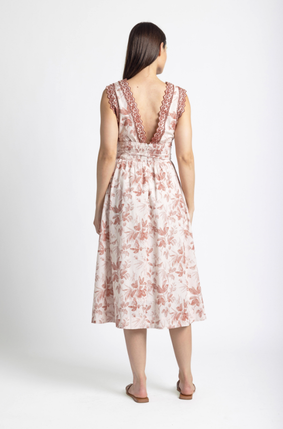 A woman wearing a beautiful pink and white Sedona Midi Dress with floral embroidery.