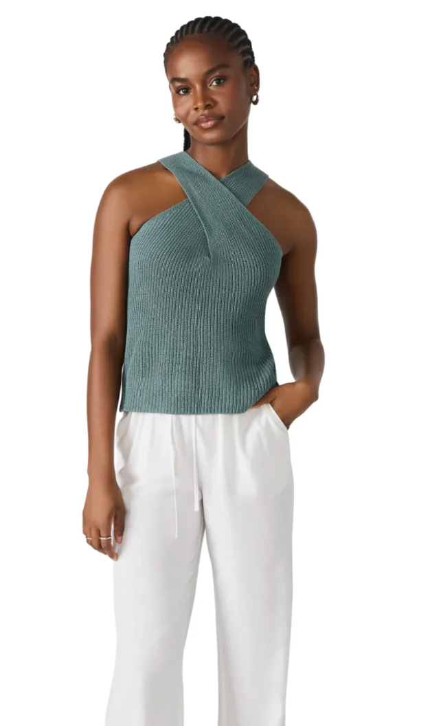 Woman wearing a green sleeveless top and white pants on a white background