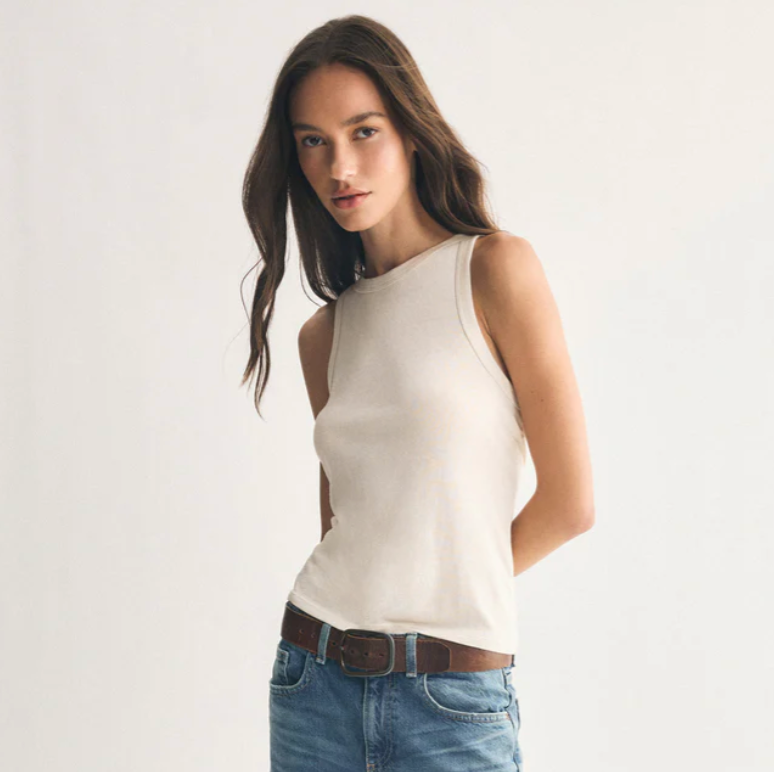 Woman wearing a white sleeveless top and blue jeans on a plain background